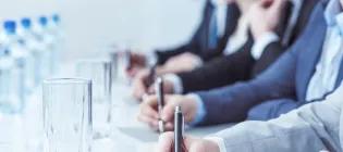 Row of people writing with pens with glasses and water bottles in front of them